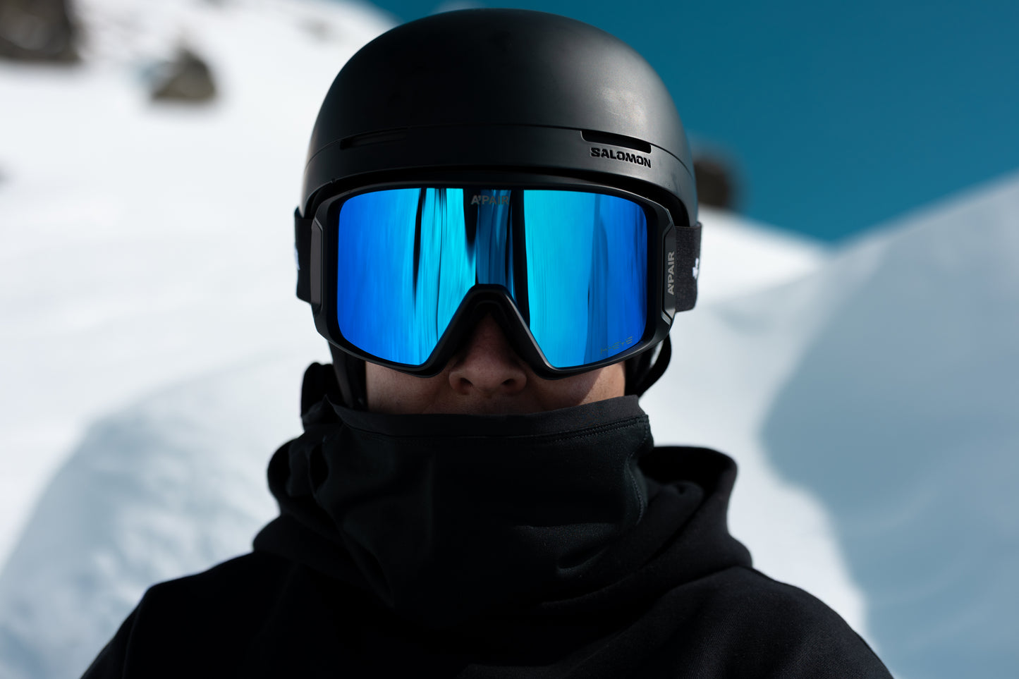 Person wearing a black helmet and blue goggles with a snowy background