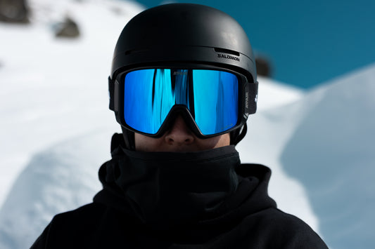 Person wearing a black helmet and blue goggles with a snowy background