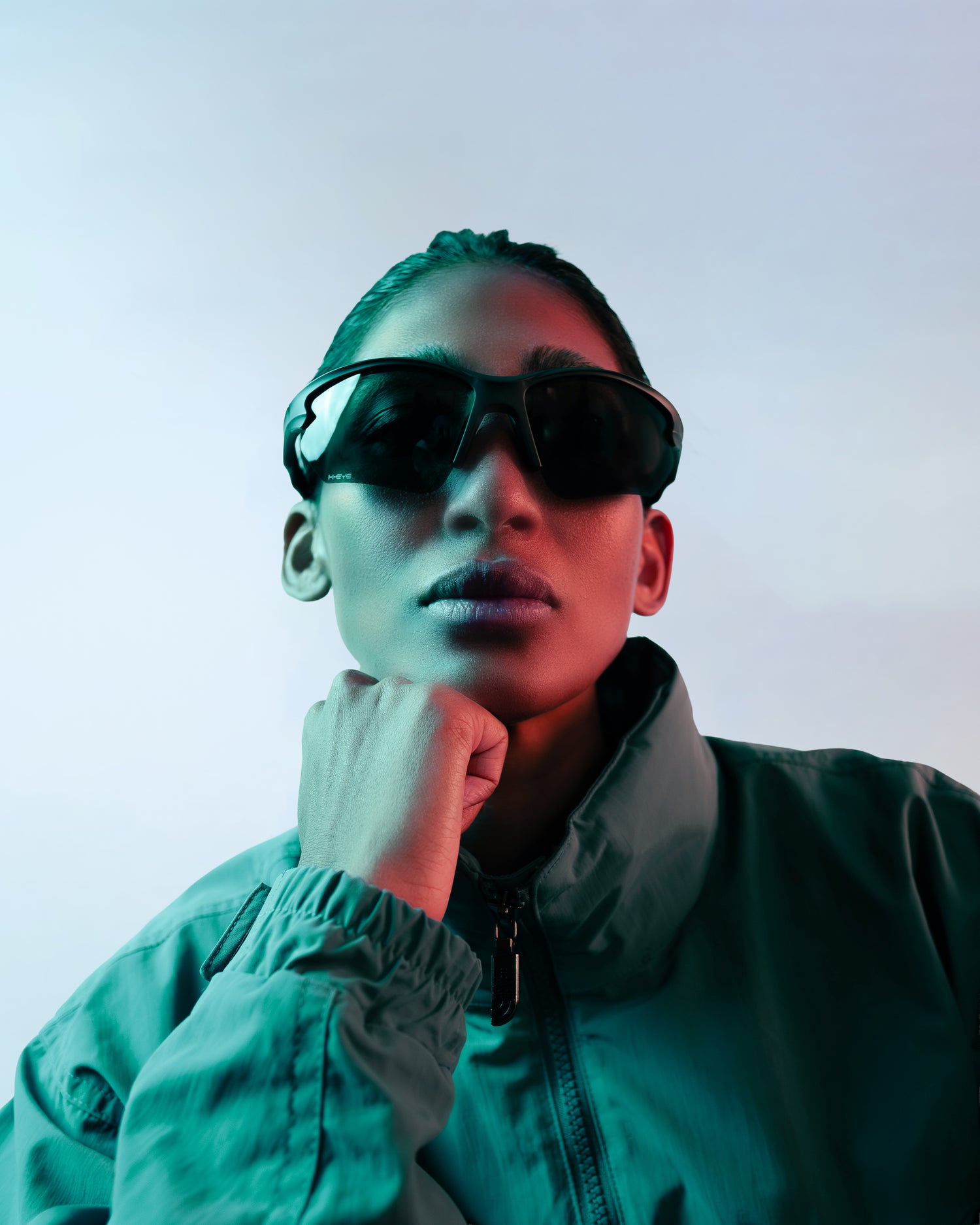 Person wearing sunglasses and a teal jacket against a light background